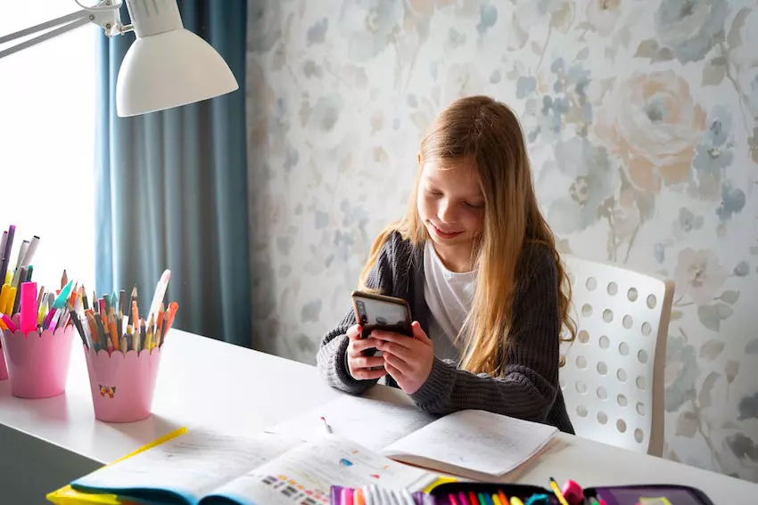 kind sitzt am-schreibtisch-mit smartphone in der hand